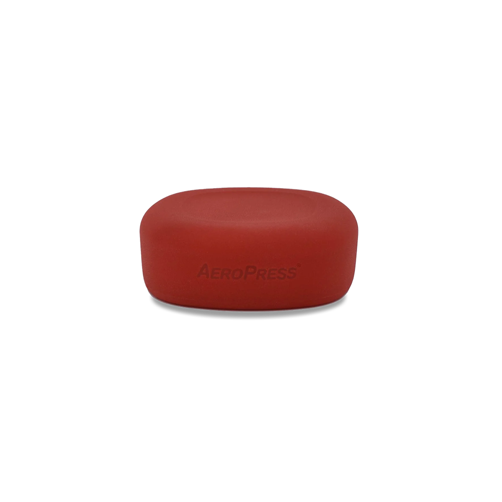 A red silicone lid with the 'Aeropress' brand name embossed on the top surface.