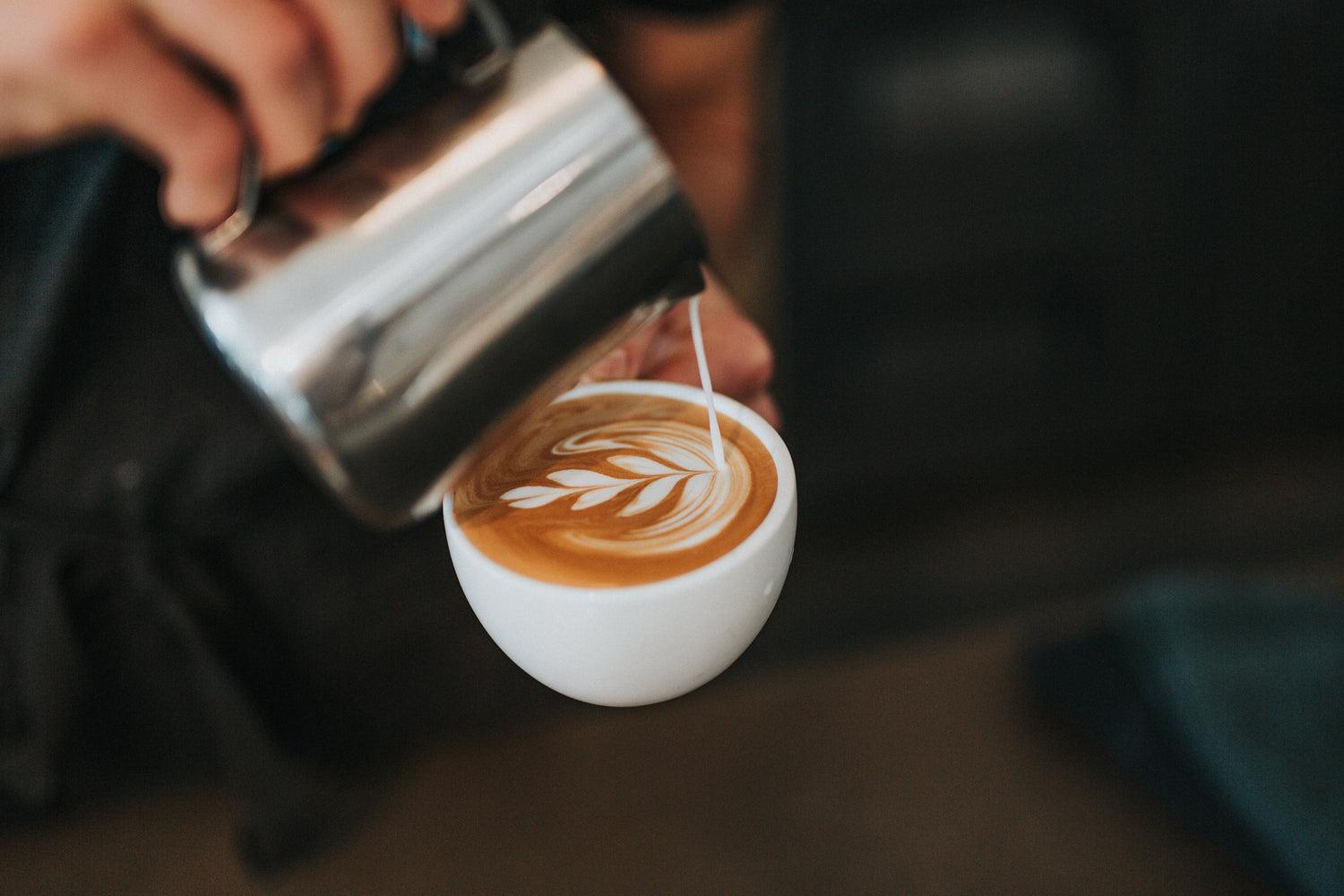 Barista pouring steamed milk into a white ceramic cup to create latte art