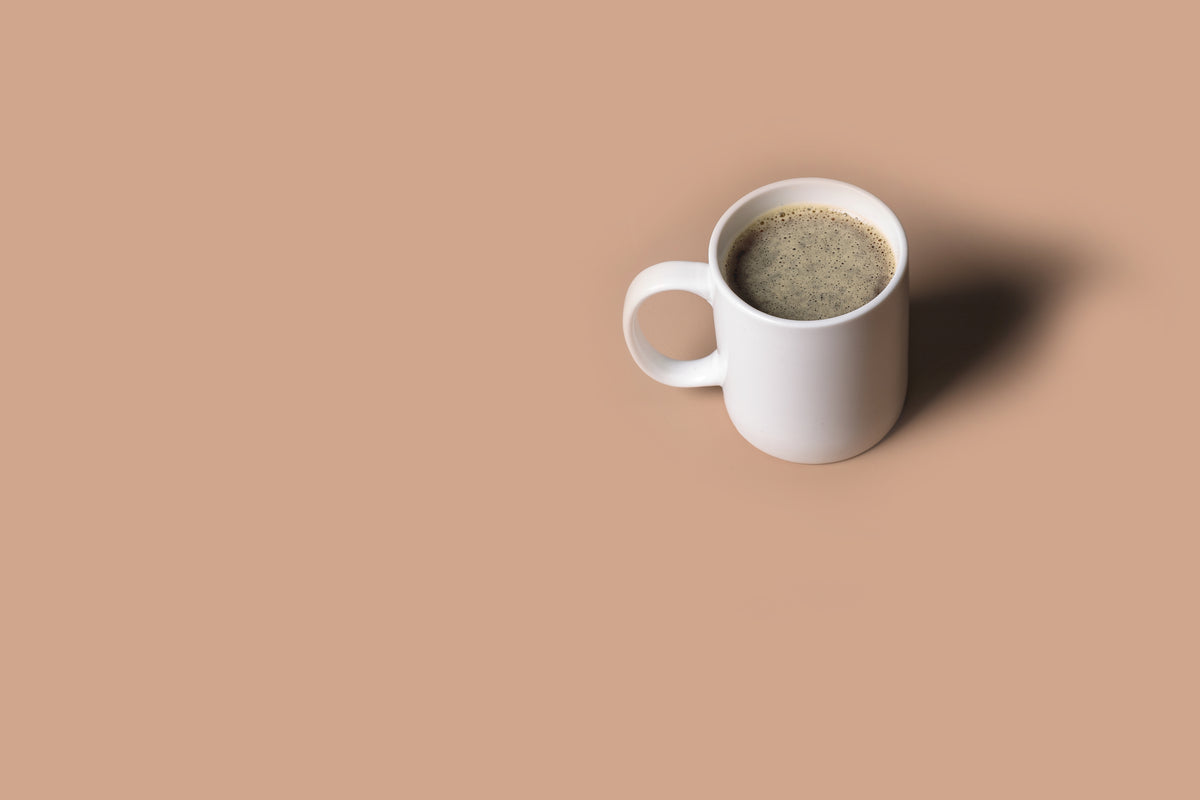 White ceramic mug filled with black coffee on a tan background